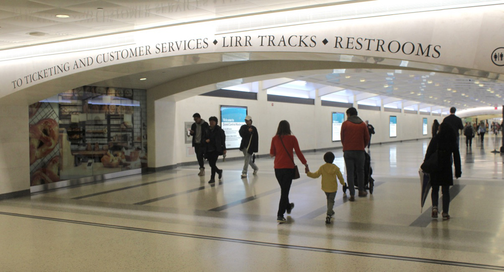 People walking under archway with signs, "To ticketing and customer services, LIRR tracks"