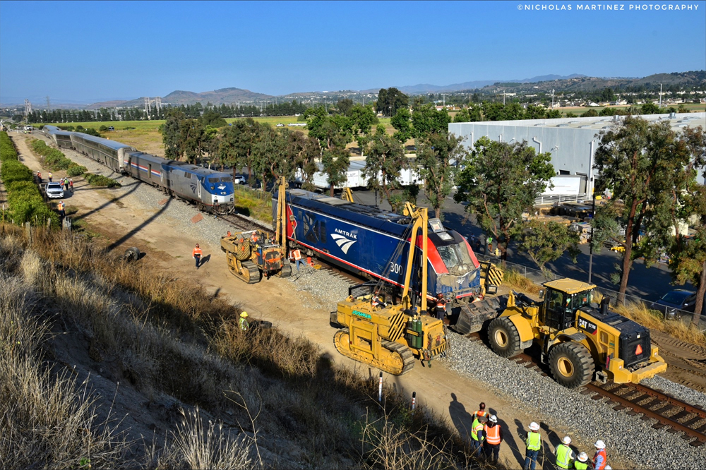 Heavy equipment lifting damaged locomotive onto railroad tracks