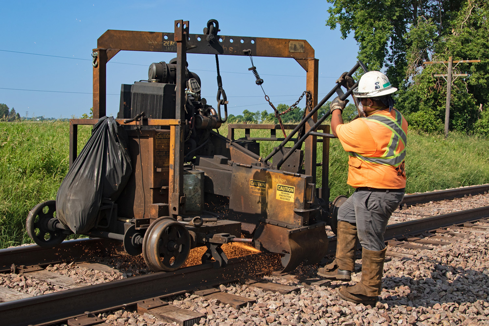 Man pushing machine along track to cut rails