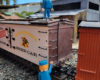 Two figures next to a model refrigerator car on a garden railway