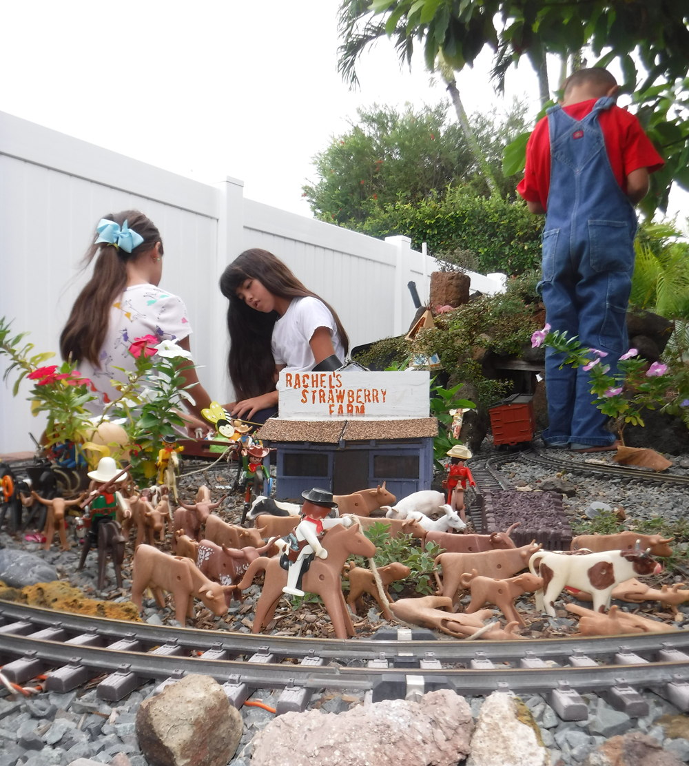 three children in garden railway with cattle figures in front