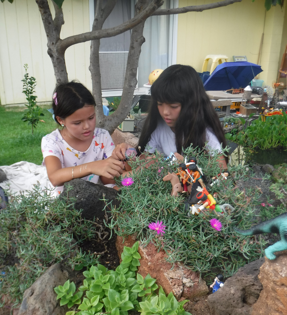 two children with dinosaur figures in garden railway