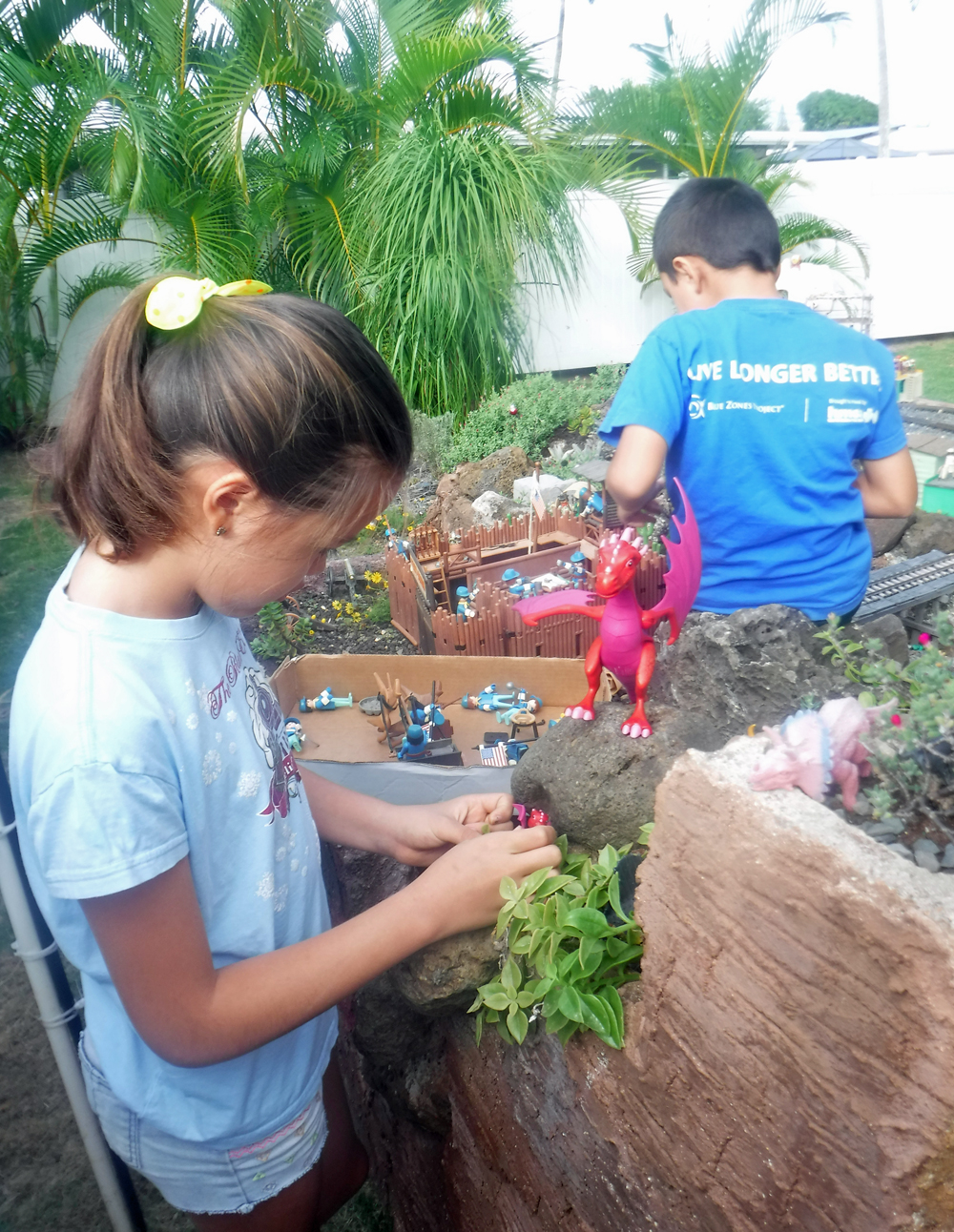 girl with pink toy dragon near garden railway