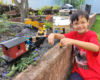 boy in red shirt smiling next to garden railway
