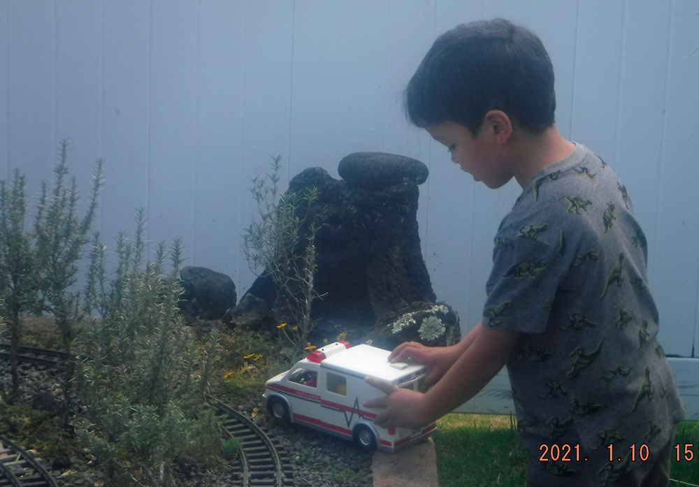 hild with toy rescue vehicle next to garden railway