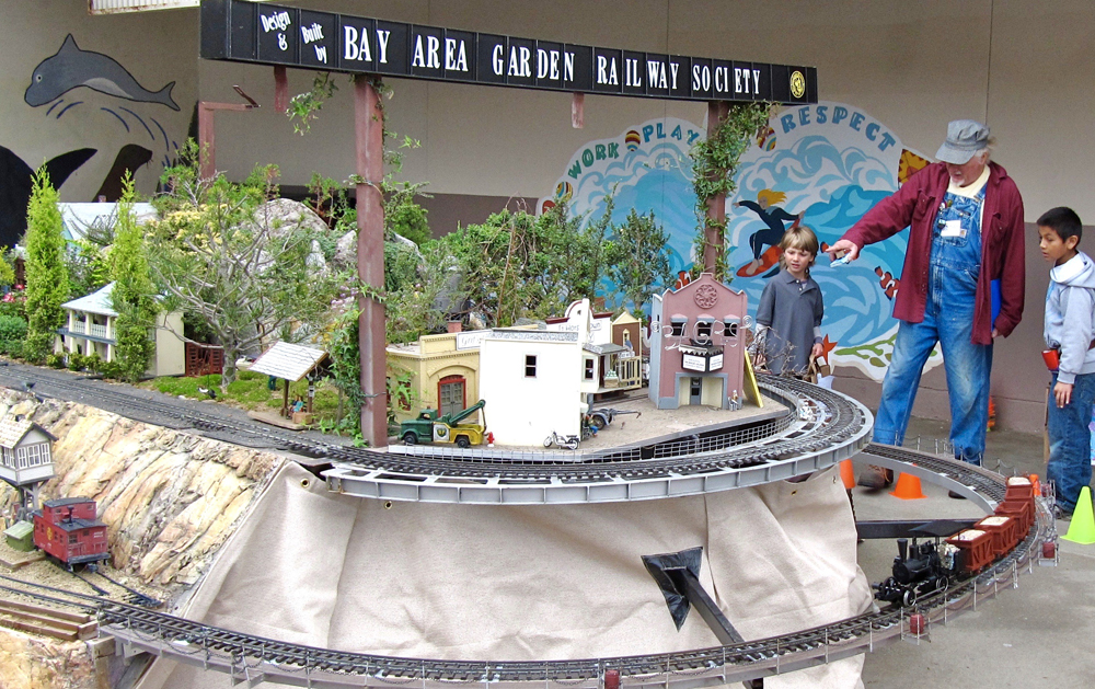 man pointing to something on a garden railway display with boy next to him