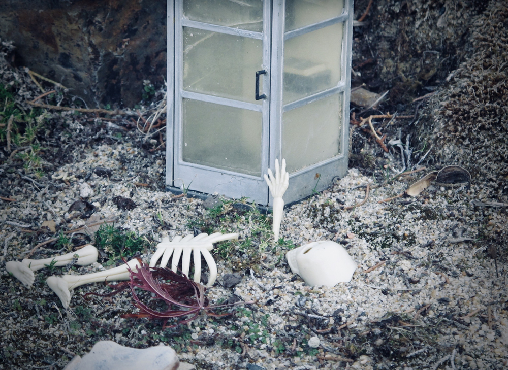 model skeleton buried next to model phone booth on garden railway