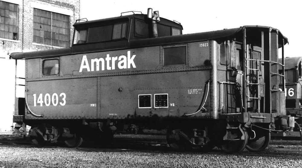 Black-and-white image of steel caboose lettered for Amtrak.