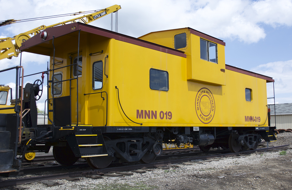 Color photo of steel wide-cupola caboose painted maroon and yellow.