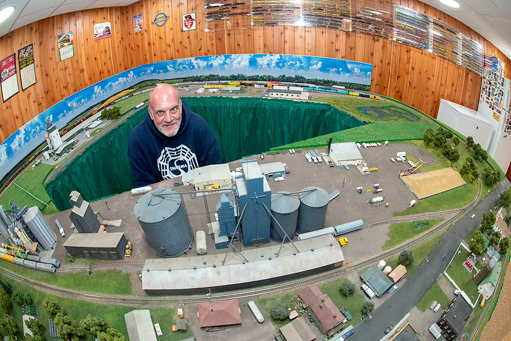 Super wide-angle photo of Mark Peterson in the middle of a model railroad.