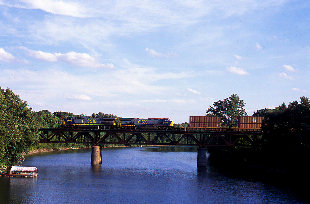 Blue, gray, and yellow diesel locomotives with freight train on bridge over river