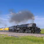 Big Boy steam locomotive rounds curve on a sunny day.