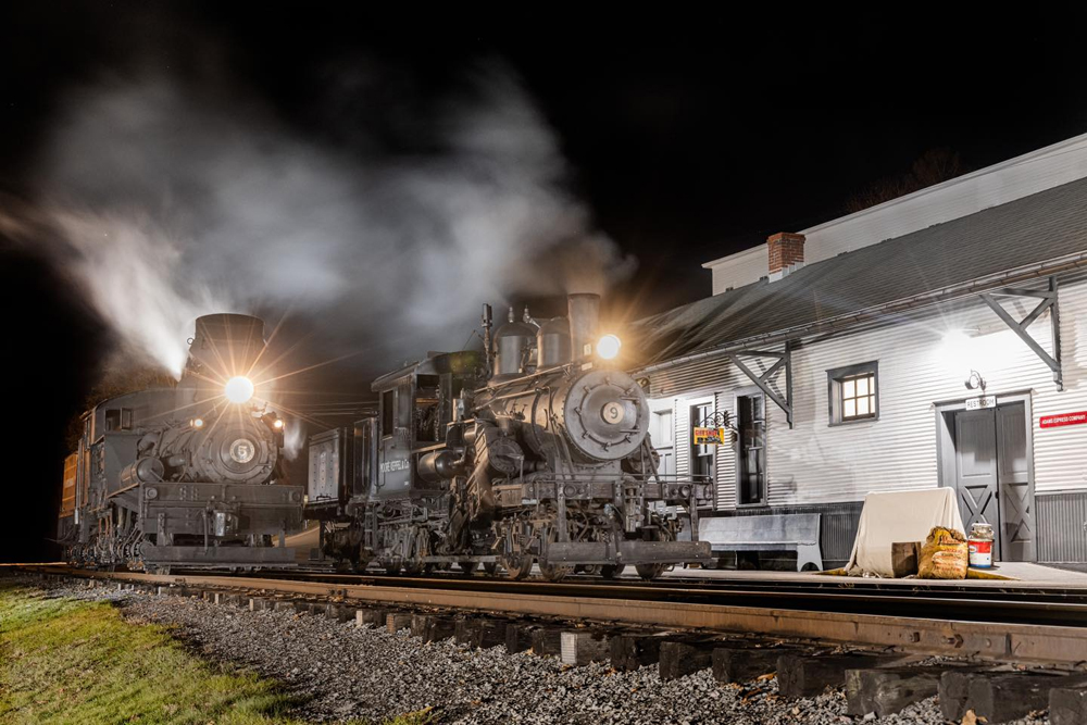 Two steam locomotives posed outside station at night 
