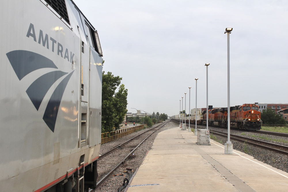 Passenger train at station platform with freight train visible in background