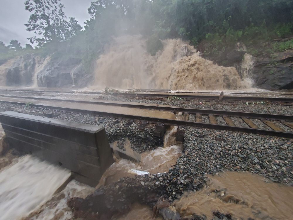Water rushing down hillside behind undermined railroad tracks