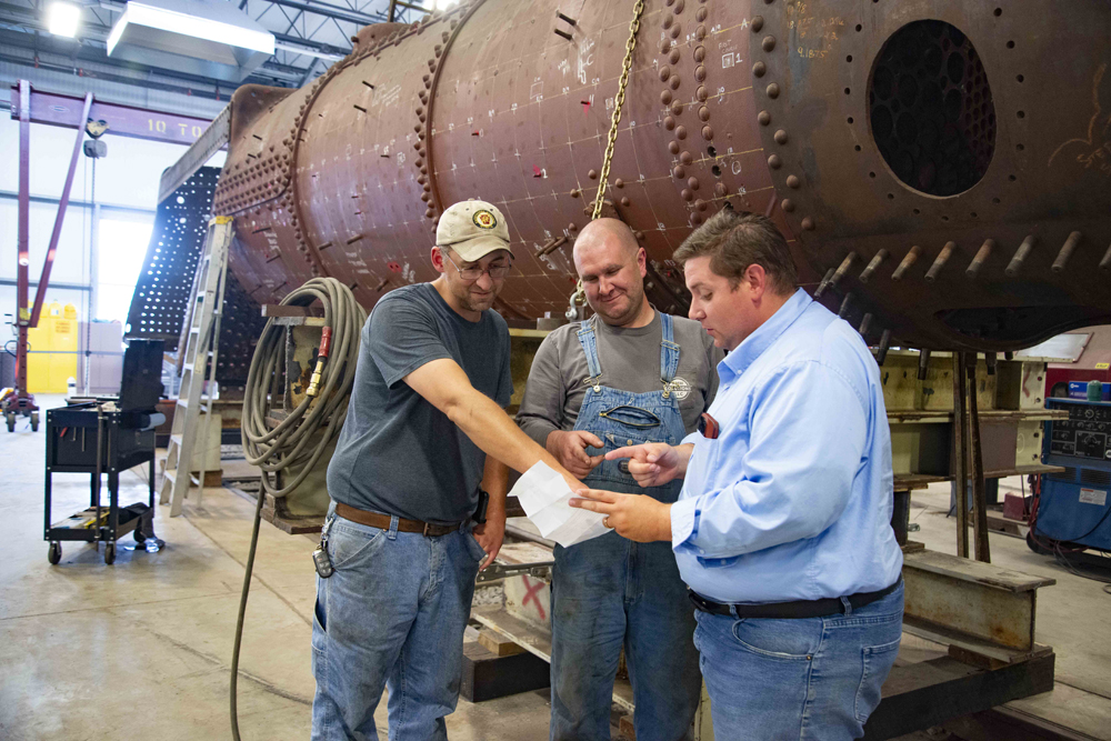 Men discuss work on steam engine behind them