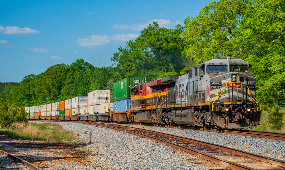 Intermodal train led by one gray locomotive and one with red, yellow, and black paint.