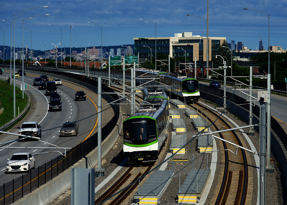 Two green-and-white light rail trains meet on tracks in center divider of highway
