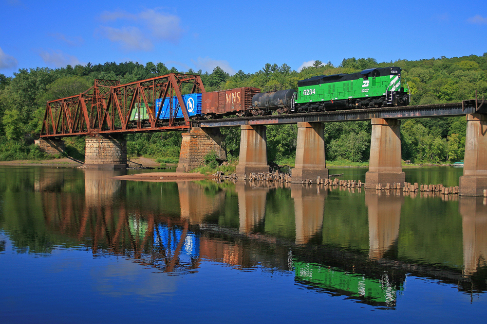 Green locomotive with short freight train on bridge