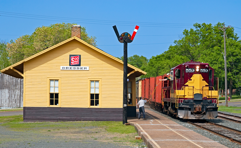 Maroon and gold vintage diesel locomotive at yellow station with semaphor signals.