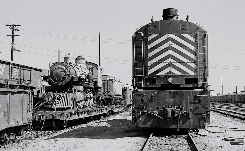 Steam locomotive on flatcar next to wrecking crane