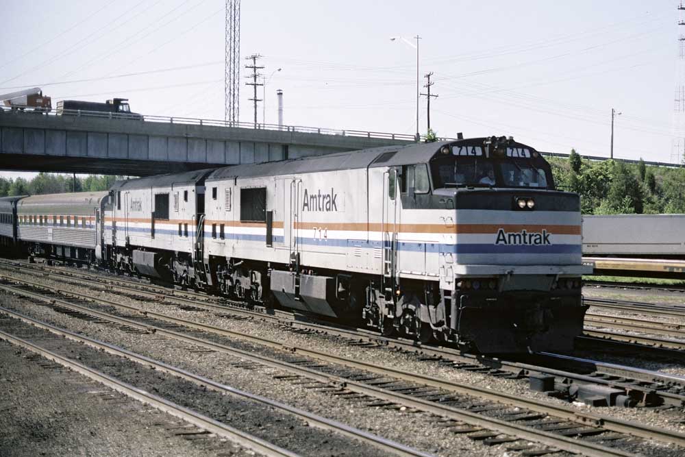 Silver-and-black Amtrak GE P30CH locomotive leads passenger train under highway bridge