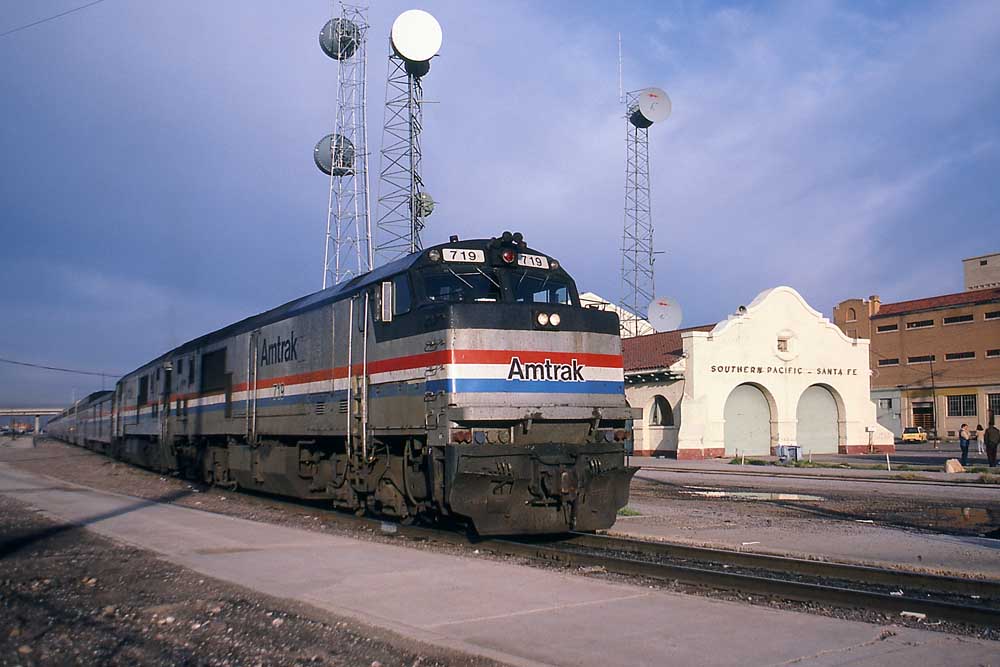 Silver-and-black Amtrak GE P30CH locomotive leads passenger by a station