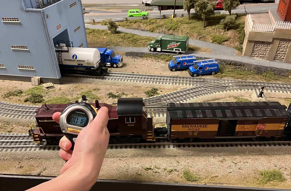 train on layout, with hand holding a stopwatch near the engine