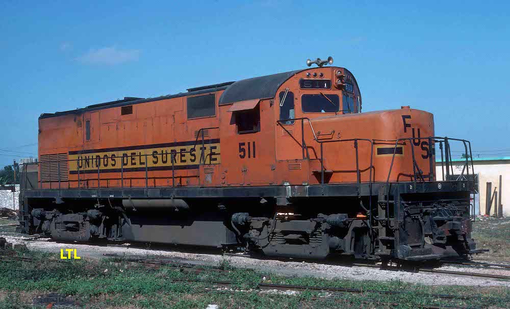 Under a clear blue sky an orange locomotive lettered for the Ferrocarriles Unidos del Sureste rests in a railyard.