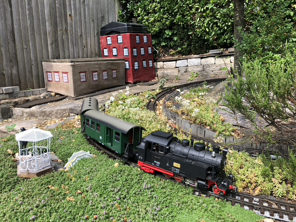 colorful model train on garden railway, with two mesh buildings in the background