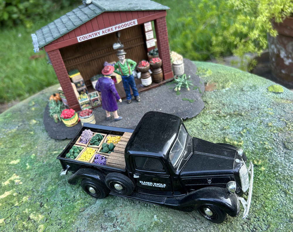model black truck with grocery load next to model grocery stand