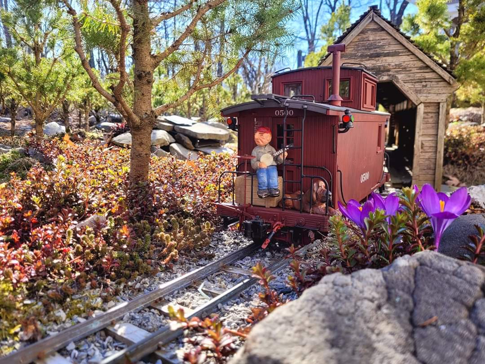 model caboose with figure and dog heading away from you on a garden railway