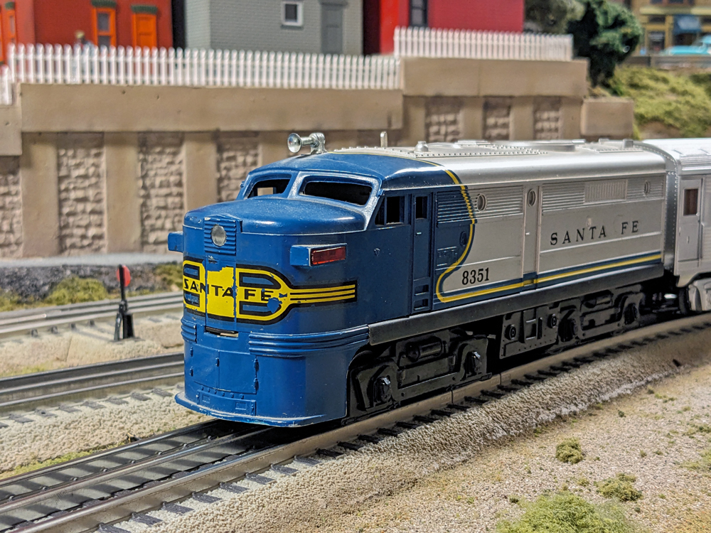 A model of a blue and silver streamlined diesel locomotive sits on the tracks with a passenger car behind it