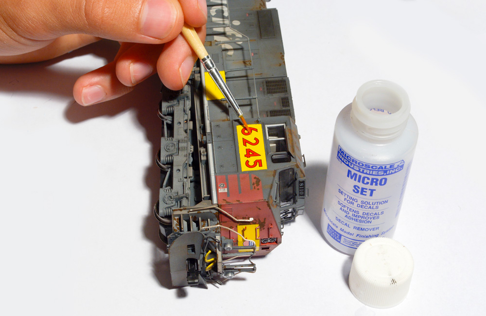 A paintbrush is used to arrange number decals on a yellow patch painted on a model locomotive
