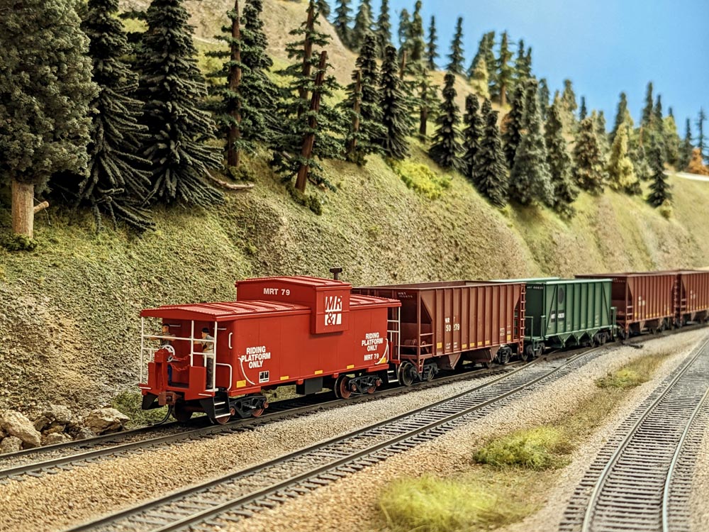A model red caboose leads a shove of hoppers