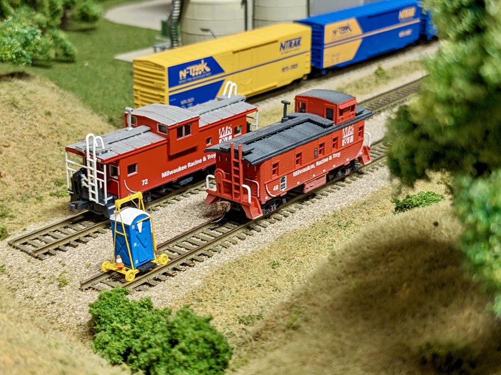 Two model red cabooses sit in a rail yard
