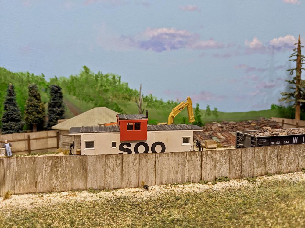 A model white and red caboose sits in a scrap yard