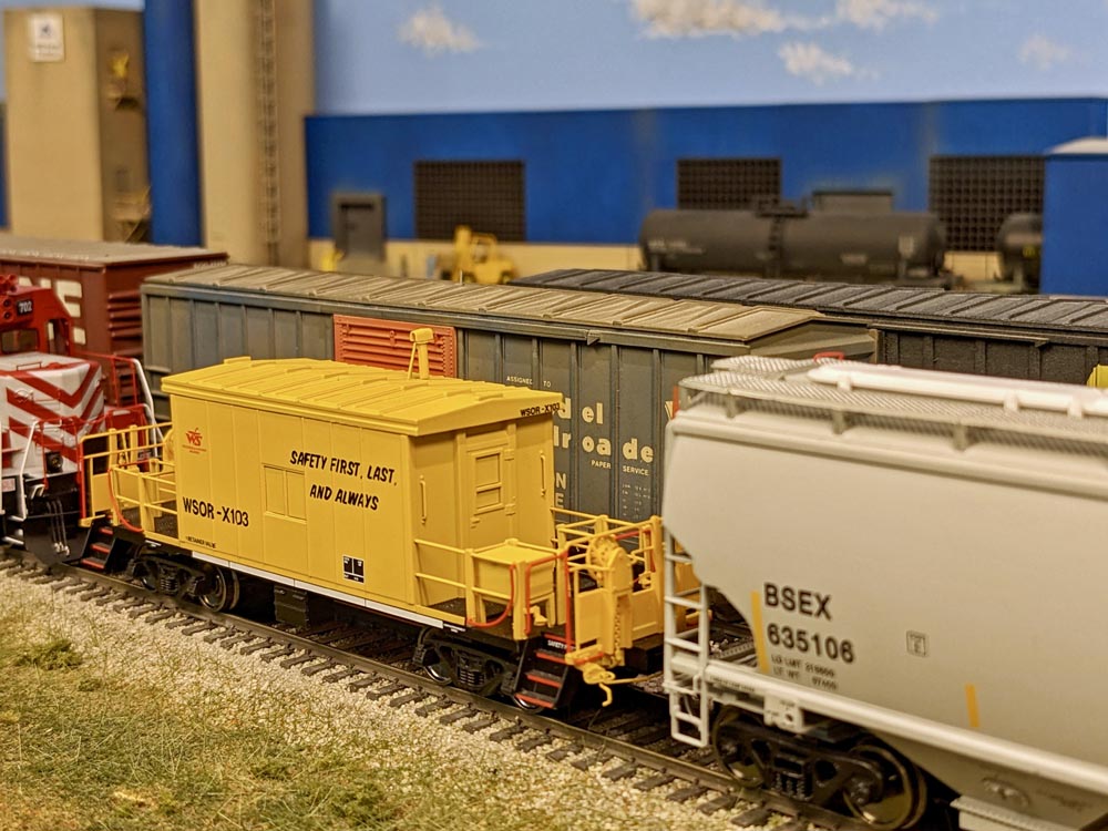A model yellow caboose between a locomotive and freight car