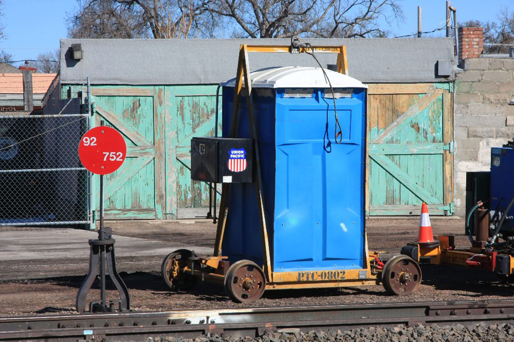 A blue porta-potty on a yellow rail cart chassis