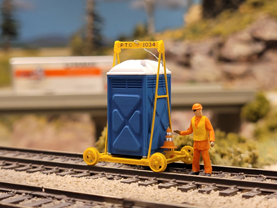 A model porta-potty on a railcart chassis with a model figure