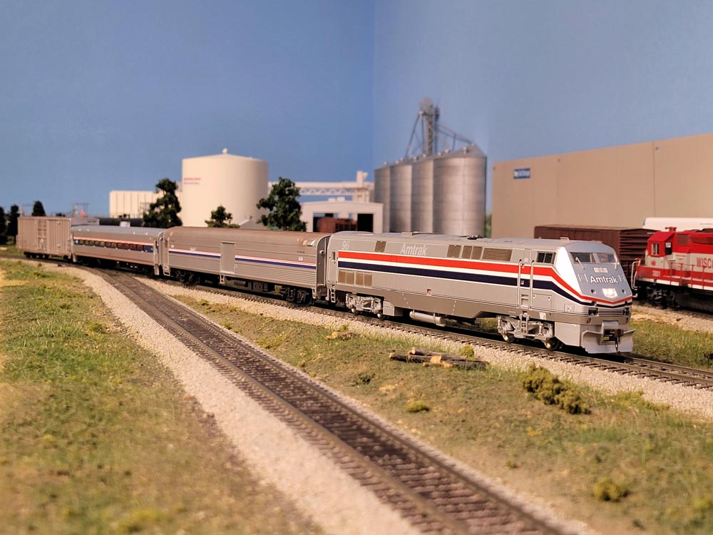 A model passenger train passes in front of an agricultural facility