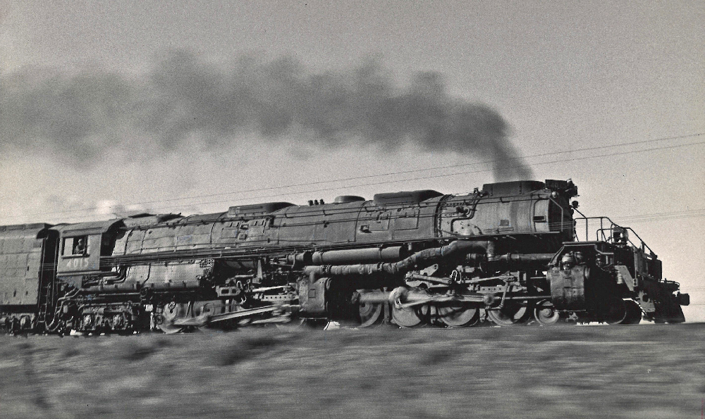 Black and white photo of large steam locomotive racing along the rails.