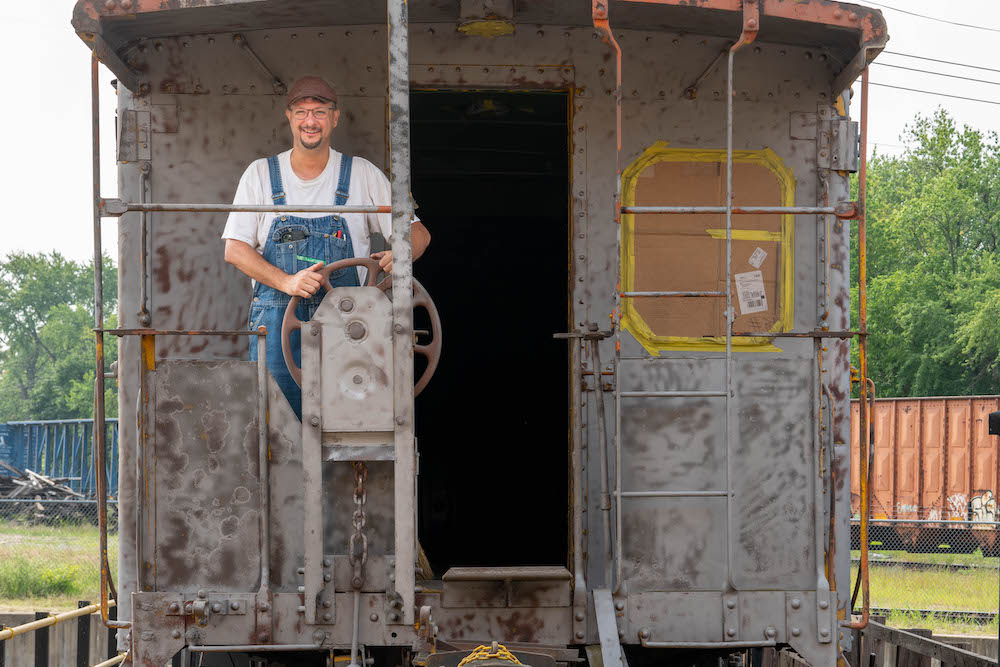 Young man stands on platform of caboose.