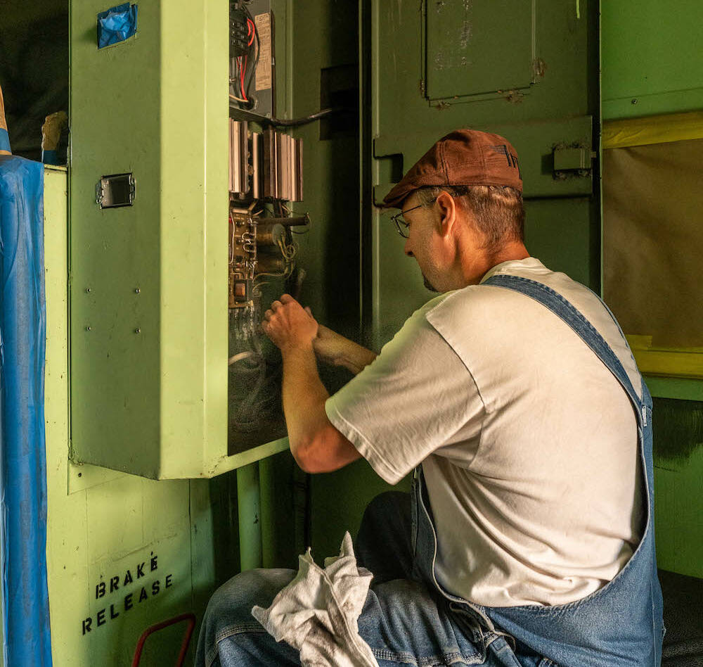 Young man works on electric box inside a caboose.