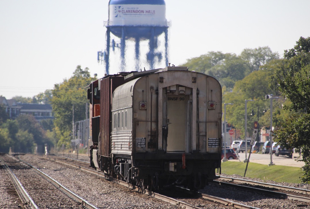 Train with locomotive, hopper car, and former passenger car, as seen in going-away view