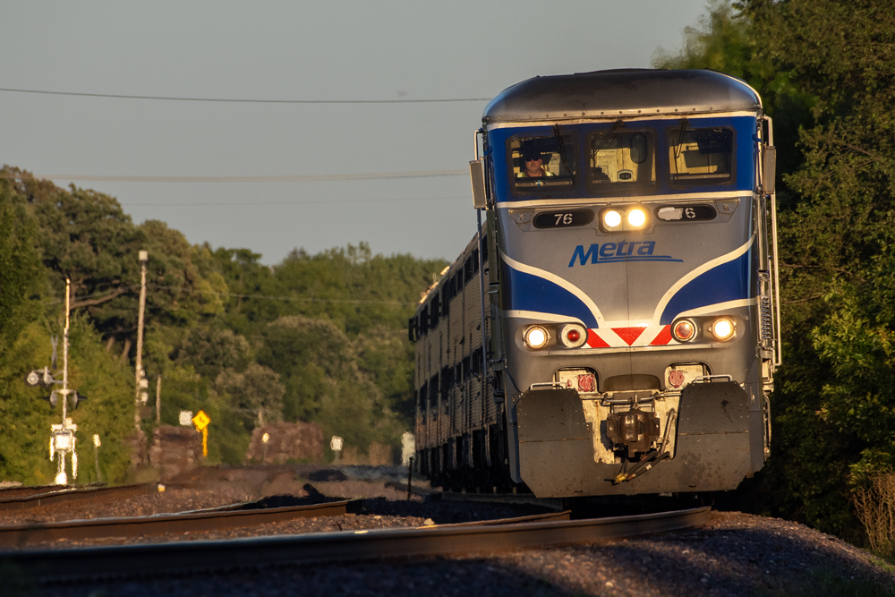 Commuter train with blue and silver engine on curve in golden-hour lighting.