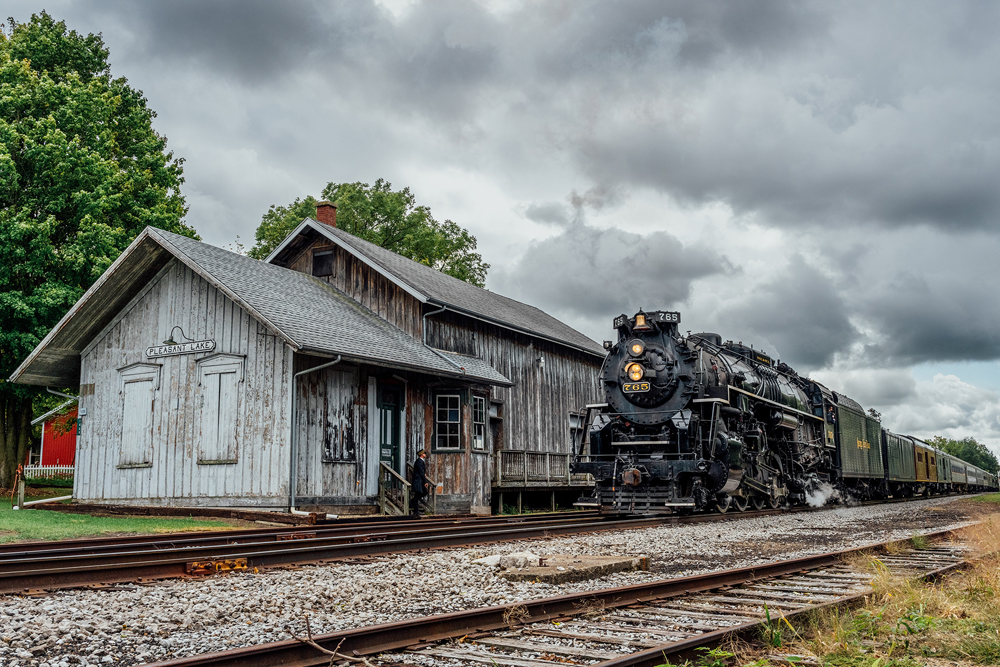 Weathered wooden railroad station being passed by steam locomotive