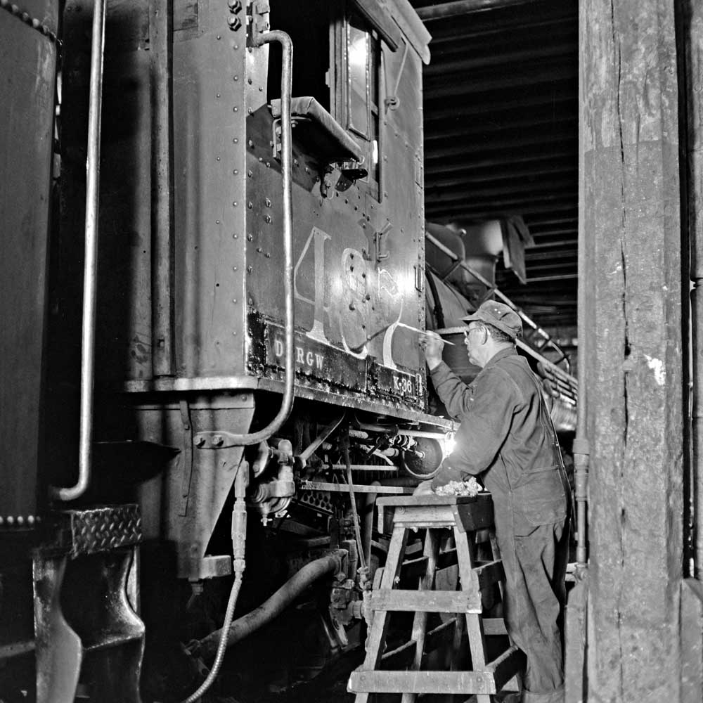 Man with ladder works on steam locomotive indoors