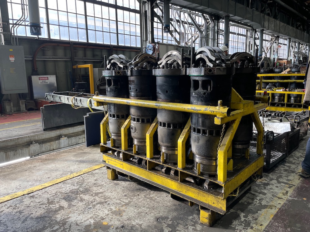 Eight grimy diesel locomotive cylinders held upright in a yellow rack inside a maintenance building