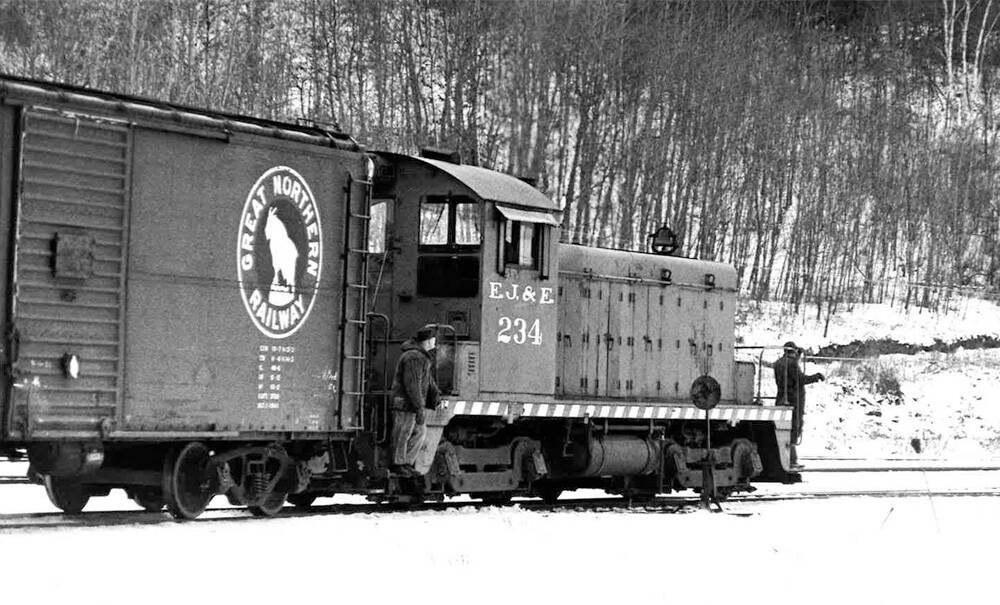 A black-and-white photo of an early diesel switcher moving a Great Northern boxcar through a snowy landscape
